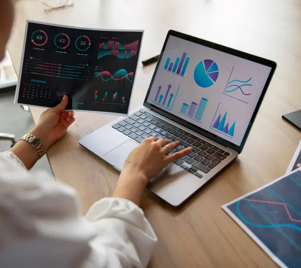 person on laptop while holding some graphs printed on paper